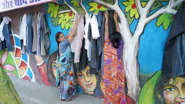 Women hang donated clothes on the wall that is giving locals a taste for charity. Photo: Gopal Kamad