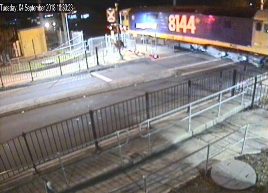 Close call: Just seconds after the man crosses, a freight train streaks past, with the lights of an oncoming southbound passenger train visible in the left-hand corner. Picture: Transport for NSW