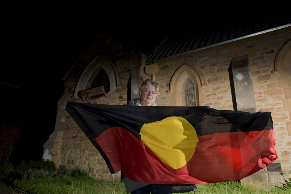Janet Bromley with one of the two flags on display at the site, which is the venue of an Indigenous art fair. The other flag is missing. Picture: NONI HYETT